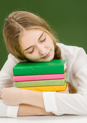 Teen girl sleeping on books in classroom