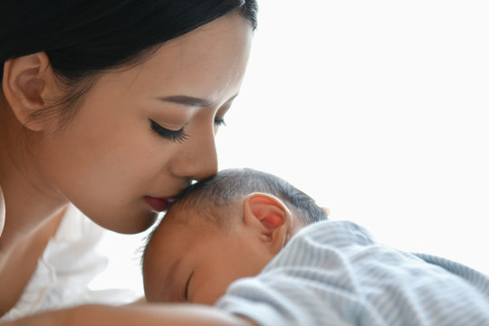 Newborn Concept. Mother and child on a white bed. Mom and baby boy playing in bedroom. Parent and little kid relaxing at home. Family having fun together. Newborn baby is fussing and crying.