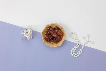 Table top view aerial image of decorations Ramadan Kareem holiday background.Flat lay date in wood basket with white rosary & lighting.Object on modern rustic purple paper at office desk wallpaper.