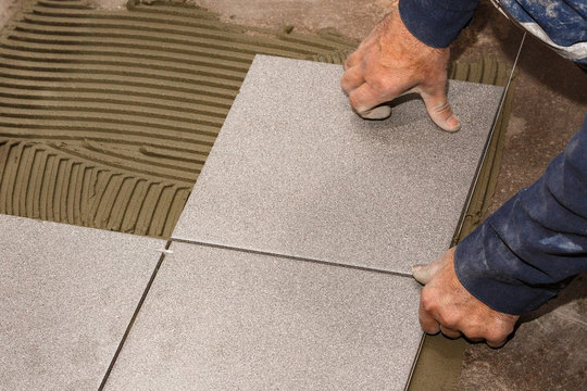 Hands of the worker lay ceramic granite on the floor. Close-up.