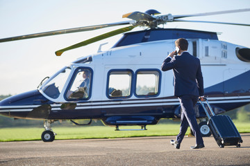 Rear View Of Businessman Walking Towards Helicopter Whilst Talking On Mobile Phone