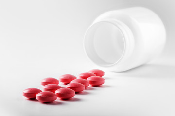 Medical pink pills and white bottle on white light background. Concept of healthcare and medicine.