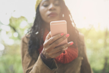 African America girl in park using smart phone. Focus on hand.