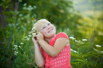 The girl is blonde among the tall flowering herbs in the summer.