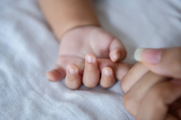 Newborn Concept. Mother and child on a white bed. Mom and baby boy playing in bedroom. Parent and little kid relaxing at home. Family having fun together. Newborn baby is fussing and crying.