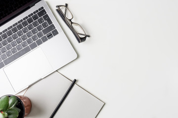 Top view of office workplace. White desk with copy space. Flat lay view on table with laptop, glasses, pen, notebook and green flower. Creative designer concept.