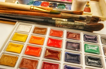 Sets of watercolor paints and various brushes on the white background 