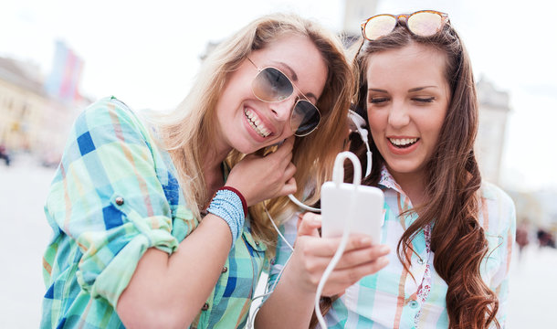 Listening to music. Two girls having fun with mobile phone and headphones. Lifestyle, fashion, technology