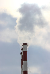 A smoke cloud from three industrial plant chimneys standing in a row against a cloudy sky