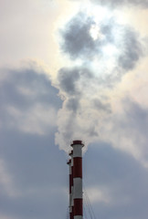 Sunshine struggling through the smoke cloud from three industrial plant chimneys standing in a row against a the cloudy sky 