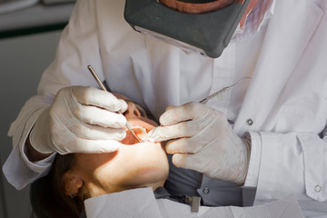Dentist with special glasses and latex gloves using calculus plaque remover tooth scraper and...