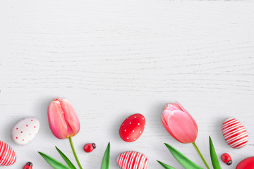 Easter eggs and spring tulip flowers on white wooden surface. Free space for text. Top view.