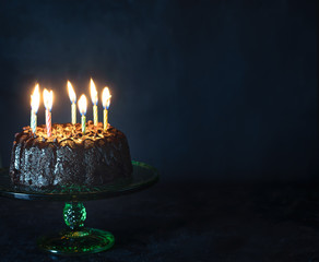 Chocolate chip cake with lit candles on dark background