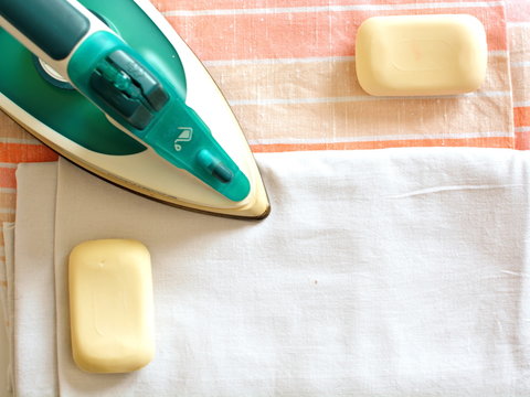 Electric steam iron presser, piece of soap and folded clean washed ironed cotton bed linen in neutral hues. Manual labor