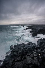 Rugged Icelandic coastline with big  waves hitting the black rocks at overcast evening in south west Iceland.