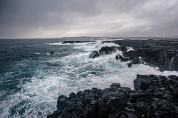 Rugged Icelandic coastline with big  waves hitting the black rocks at overcast evening in south west Iceland.
