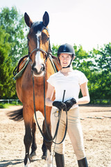 Young teenage girl equestrian standing with her favorite red horse