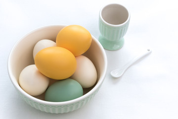 Fototapeta na wymiar Yellow and Mint Easter Eggs in Green Bowl on White Linen Background with Eggcup and Salt Spoon