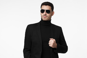 Tough bodyguard or secret agent wearing suit and sunglasses, isolated on grey background