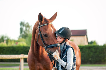 Young teenage girl equestrian kissing her favorite red horse