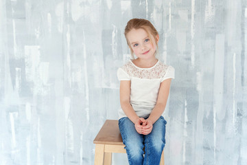 Sweet happy little girl in blank white t-shirt sitting on chair against grey textured wall background