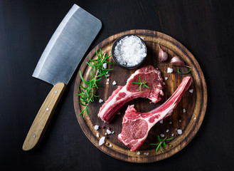 Two raw lamb chops on a wooden cutting board with spices on a dark wooden background © Ekaterina Belova