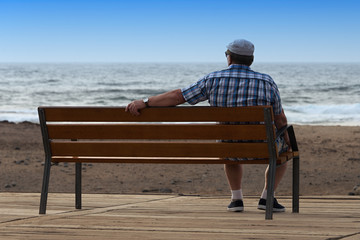 Pensioner sitting on a bench and looking at ocean
