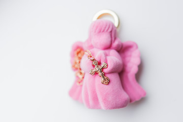 Golden cross for christening on pink gift box in shape of praying angel. Elegant religious accessory for little baby girl. Russian Orthodox church ceremony details.