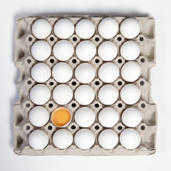 One broken egg with the other white eggs in a cardboard box from the store. It looks like a chessboard.