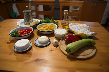 Ingredients for the preparation of vegetable pasta, at background of a wooden table and rustic plates.