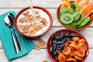 Milk is poured into  bowl with flakes. Dried kiwi, mango, apricots and raisins, healthy food.