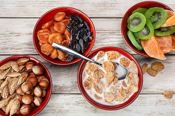 Products for healthy breakfast. Wooden bowls with nuts, dried fruits. Cereal flakes with milk.