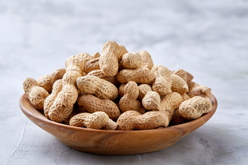 Unpeeled peanuts in wooden bowl over rustic wooden background closeup, selective focus