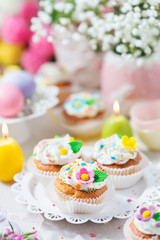 Easter cupcakes with sugar flowers, pastel color eggs and candles on a light background