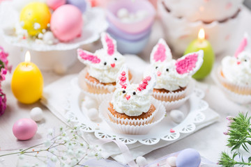 Bunny cupcakes with white cream, flowers and colorful eggs. Easter background