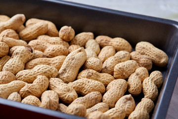 Unpeeled raw peanut on baking tray over white textured background, selective focus, shallow depth of field.