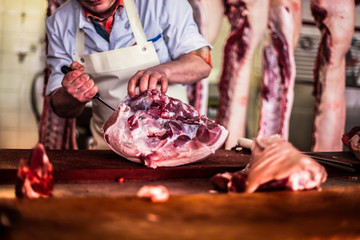 butcher cut raw meat of a pig with a knife at table in the slaughterhouse