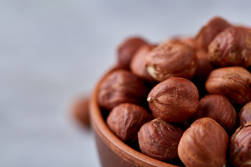 Hazelnuts in wooden bowl on wihite background with copy space, top view, selective focus.