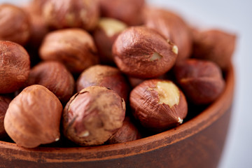 Hazelnuts in wooden bowl on wihite background with copy space, top view, selective focus.
