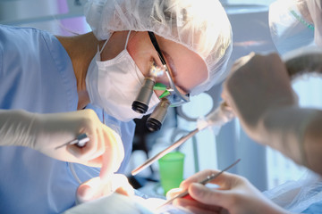 Female dentist and assistant in surgical uniform at the clinic in the treatment of a patient