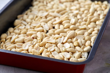 Peeled peanut on baking tray over white textured background, selective focus, shallow depth of field.