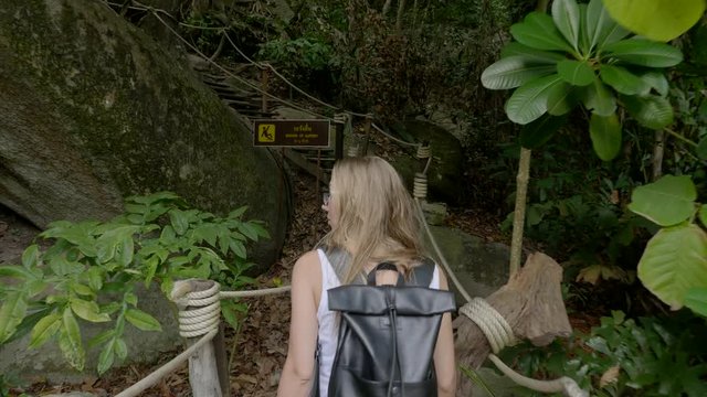 Young blonde girl walking along pathway and wood roots in the tropical rain forest or jungle. Beauty in nature,active woman, healthy lifestyle concept.