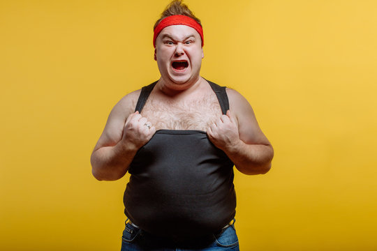 Furious fat man wearing red headband and black shirt screams on dark background