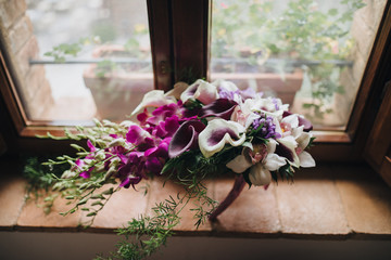 bouquet of red, white flowers and greenery stands on windowsill of an old house with wooden windows and shutters