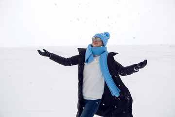 Fototapeta na wymiar girl in winter clothes standing on a frozen lake throws up snow