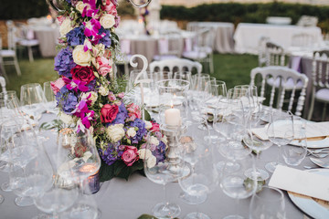 the flower arrangement stands on the table in the wedding banquet area on a green glade, the table is decorated with candles, there are plates, glasses, cutlery