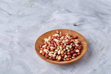 Raw mixed peanuts in wooden plate isolated over white textured background, top view, close-up.
