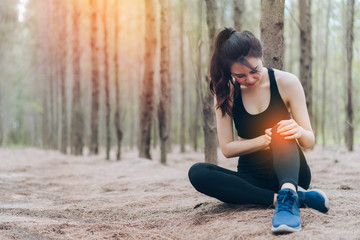 Asian woman injury knee after training exercise runner workout marathon at forest sitting pain healthy lifestyle concept.