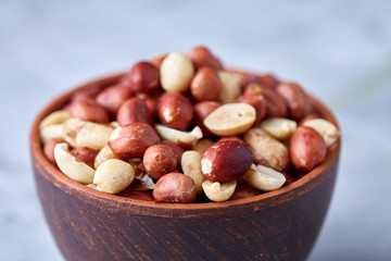 Raw mixed peanuts in wooden plate isolated over white textured background, top view, close-up.