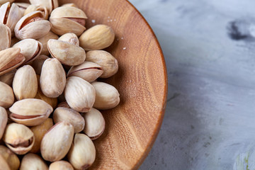 Salted pistachios on a wooden plate over white background, top view, close-up, selective focus.
